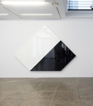 Large geometric wall artwork composed of a white and a glossy black surface in an exhibition space.