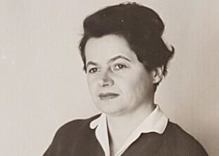 Woman with her hair up, white shirt collar, and dark sweater looking slightly sideways.