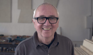 A smiling older man wearing black glasses in a studio.