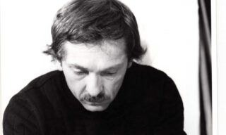 Man with mustache and dark sweater looking down intently.