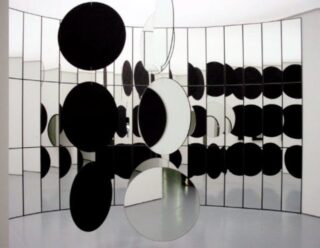 Installation with large, round hanging mirrors in front of a tall mirrored wall, creating multiple reflections of the round mirrors.